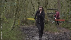 Three women running through a mud run / assault / obstacle course. They are racing through the muddy track, competing