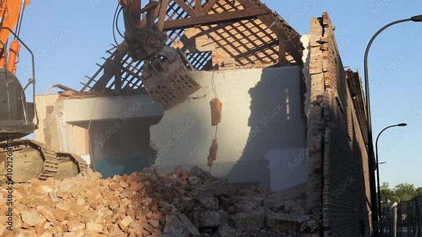 Demolition of an old brick building in the city at sunset with heavy machinery working