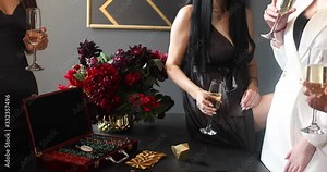 Pretty young women in cocktail dresses talking and holding glasses of champagne while playing poker. Game concept. Slow motion