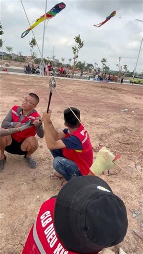The wind is so strong while flying kites that the guys have to sit on the ground to hold the stri...