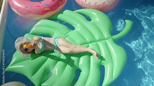 TOP DOWN: Cute girl lying on a floatie splashing with water gun towards camera. Cheerful little girl floating in backyard swimming pool and having fun with water blaster spraying in camera direction.