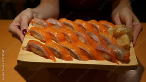 Woman hold wooden plate full of salmon sushi, put down on table. Large set of tasty nigiri served at Tokyo restaurant. Freshly cooked Japanese food, slices of salmon harasu (belly) on rice