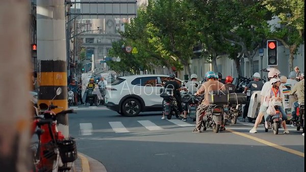 Busy city intersection with scooters, delivery riders and commuters waiting at red light while cars turn through crosswalk parcels, helmets, smartphones and treelined sidewalks create bustling