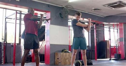 Diverse male trainer guiding male athlete through arm swings, crossbody stretches for warmup