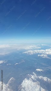 View from an airplane window on the snow capped mountain peaks of the alps in Europe. Alps in Italy, Austria, Switzerland. Plane wing flying through the clouds. Aerial view. Traveling by plane.