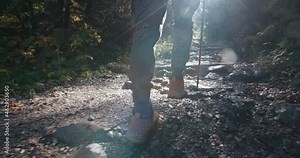Slowmotion male hiker tourist in boots going up along stone trail in mountain forest using trekking poles. Man hiking in woods walking rocky footpath. Adventure travel tourism concept