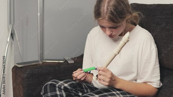 Young woman assembles a recorder at home, carefully putting together the pieces and preparing to play. Focused and dedicated, she engages in a musical hobby and learning experience