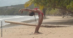 Contortionist bikini girl bends into a contortion position in the sand of an amazing beach location
