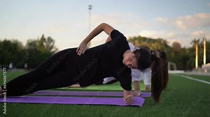 Group of sports women does side plank exercise to strengthen body on green turf flooring. Women enjoys training on sports ground near city park