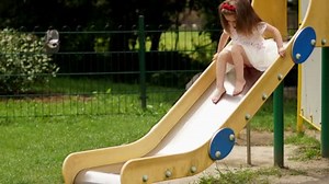 Outdoors Portrait of Cute Little Girl Playing on the Childrens Slide on the Playground During Summer Sunny Day.