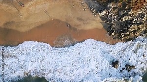 A man lays on a beach and makes sand angel in the sand as seen from an overhead drone