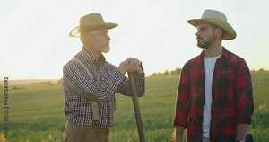 Full length view of the senior farmer engineer coaching young intern farming technologies. Mature specialist telling something to his colleague. Off season harvest and agronomy concept
