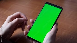 The green screen of a smartphone or chroma key. Women's hands hold the phone, click the touch screen. Close up Mock up