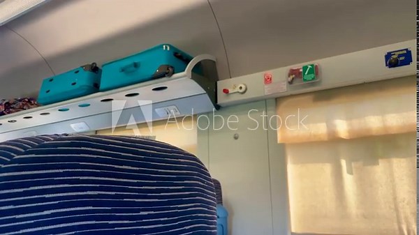 Inside Train Interior: An intimate view inside a train, showcasing a shelf holding baggage, a display of control panels, and glimpses of passengers. Captures the essence of travel.