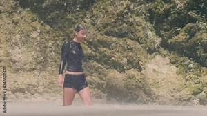 Carefree woman in wet clothes enjoying water drops falling from mountain waterfall in jungle. Atrractive girl in mountain lake under water flowing from tropical waterfali in rainforest.