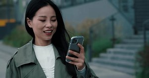 clip-3394383113-asian-girl-walking-city-while-typing-on