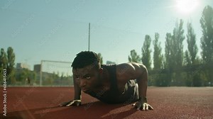 Motivated African American sport man athlete bodybuilder doing push ups exercise on football stadium male young sportsman fitness trainer in city training arms biceps muscles summer workout outdoors