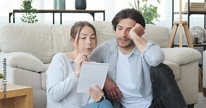 Thoughtful couple planning and writing shopping list in notepad at home