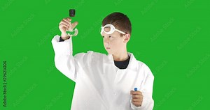 Boy scientist wearing white lab coat performing science experiment on background green screen.