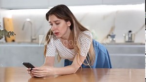Bored middle-aged woman bending over table looking thoughtfully at her mobile phone