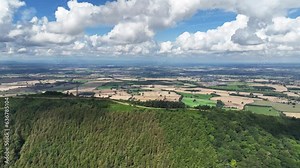 4K drone shot establishing a countryside location with a reveal of fields and clouds behind a large hill mountain terrain in england on a sunny summers day