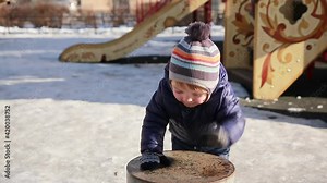 A little boy enjoys the coming spring and the warmth, walking along the street in the courtyard. A child on the playground plays a drum. Happy carefree childhood
