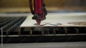 A close-up of a laser wood cutting machine cuts a particle board, smoke and fire appear. Laser beam for high-precision cutting of plywood sheet. Modern wood cutting technology.