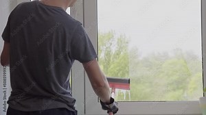 Man washes the windows with special foam and cleans them. Cleaning service. Worker in black gloves cleaning window with rag, scraper and cleanser spray at home. High quality FullHD footage