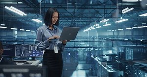 Asian Software Developer Analyze System Performance Metrics on a Laptop Inside a Modern Data Center. Young Female Manager Ensuring Efficient Operations for Critical Infrastructure