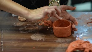On a wooden crafting table, a youngster is creating clay shapes.