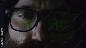 Bearded hacker in eyeglasses working on computer in the night green programming binary Matrix code reflecting on eyeglasses, close up 4k shot, technology concept