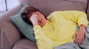 Stomach ache, pms and unhappy woman on a sofa suffering with problem, endometriosis or discomfort. Abdomen, belly and pain by girl with digestion issue, bloated and menstruation cramps in living room