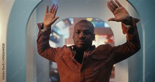 Black Man in Terracotta Button Down Shirt Stands Inside State of Art Millimeter Wave Scanner. Male Calmly Raises Hands as Part of Mandatory Pre Flight Screening Process. International Travel Safety.