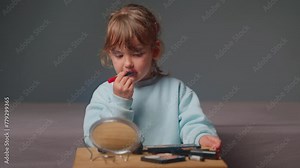 Cute little girl trying on lipstick for the first time and looks at himself in the mirror. Happiness, fun, entertainment