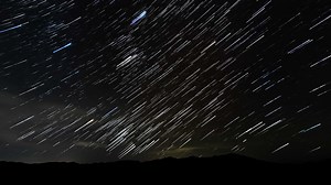 Time lapse of comet-shaped star trails in the night sky. Silhouettes of trees 4K