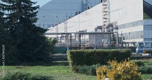 The bus carries workers to the Chernobyl nuclear power plant. Against the background of the hangar shelter from radiation. Enterprise, large building, chimney and spruce. Daytime, blue sky.