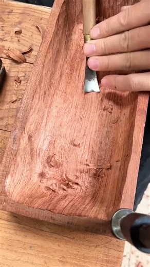 carving a dark brown wooden box manually using a silver metal chisel tool to make it very neat work