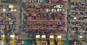 container ship and tugboat at commercial port loading and unloading cargo from container ship import and export by crane for distributing goods by trailers transported 4k top view camera up from drone