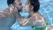 Playful couple kissing and holding hands underwater in swimming pool