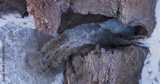 Overhead aerial view of a powerful flash flood waterfall crashing down into the Kidron River canyon in the Judean Desert during winter storms.