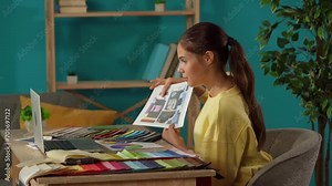 Medium shot capturing a woman working in her home office. Young designer is getting a videocall with colleagues or clients, presenting ideas and textile color samples for the project.