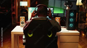 African american player in neon illuminated apartment paying close attention to computer screen during videogame competitive match. Person competing in internet esports tournament, camera B