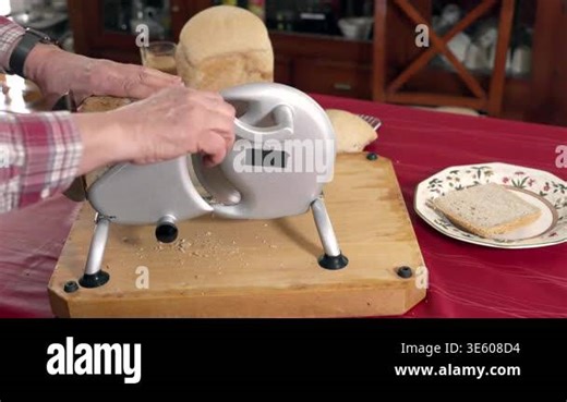 Close-up of slicing homemade bread with manual slicer on kitchen table. Fresh loaf cut into even slices, crumbs falling on wooden board Stock Video Footage - Alamy