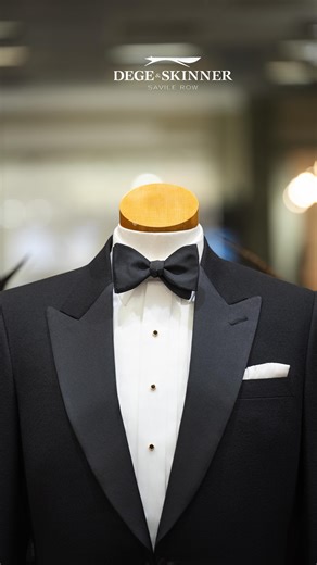 And now, a fourth twist on traditional black tie! This black barathea, single breasted dinner jacket with silk satin peak lapels has turnback cuffs in silk satin with a worsted wool Russia applied, forming an elegant and eye-catching knot design. Fastened on a link button, this dinner jacket has been paired with a ready-to-wear white poplin pleated shirt, black silk satin bow tie and gilt dress studs with black inlay. Over the years, turnback cuffs (also referred to as the cocktail cuff) have pr