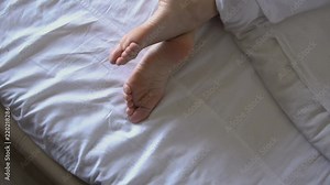 Delicate female feet moving toes playfully on white bedding. Female legs in bed view from above, white bedding Stock Video
