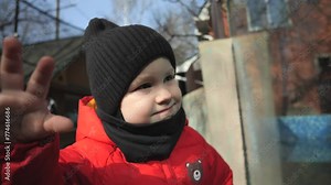 A kid wearing a red jacket walks through the zoo and looks at the animals through the fences