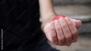 A close-up shot of a hand squeezing a red stress ball, demonstrating a common method of tension relief. The fingers press firmly, showing the effort and release of stress.
