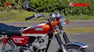 本日ご紹介するのは、90ccという小排気量ながら2気筒エンジンを搭載したHX90です。以前ご紹介した事もありますが、このモデルのルーツは1965年に発売されたAT90まで遡ります。当時のモデル名の決め事に従うと90ccは"H"を使うところでしたが、世界初の分離給油方式(Autolube)を採用した90cc初の2気筒(Twin)という特徴を強く訴求する為に、敢えてその頭文字を連ねて"AT"と命名したのだそうです。その後､1968年にはエンジンの基本部分は変えず、ツインキャブレター 5速ミッションに鋼管ダイヤモンドフレームというスポーツ指向の強いモデル、HS-1として生まれ変わりました。そのHS-1もマイナーチェンジの際に一時HS90という名称に変わりましたが、70年代に入って2サイクルロードスポーツ車の名称がRX350,DX250のように"X"を冠するようになると同時に、デザイン一新してHX90として生まれ変わったのです。この90cc2気筒エンジンを搭載したモデルは、その独特な高周波サウンドから、"ジェットツイン"とも呼ばれ、颯爽と街を駆け抜ける姿は当時の若者達の憧れの的でした。 | Y