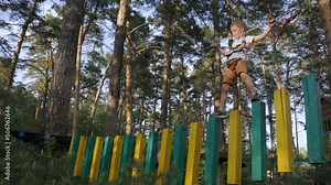 Boy walks across the inverted sleepers of the dangling bridge of the rope park high above the ground. With a difficult section of the track easily copes with a child lover of extreme entertainment