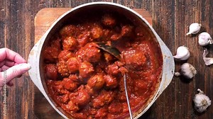 overhead view of ladle stirring large pot of homemade meatballs and spaghetti sauce
